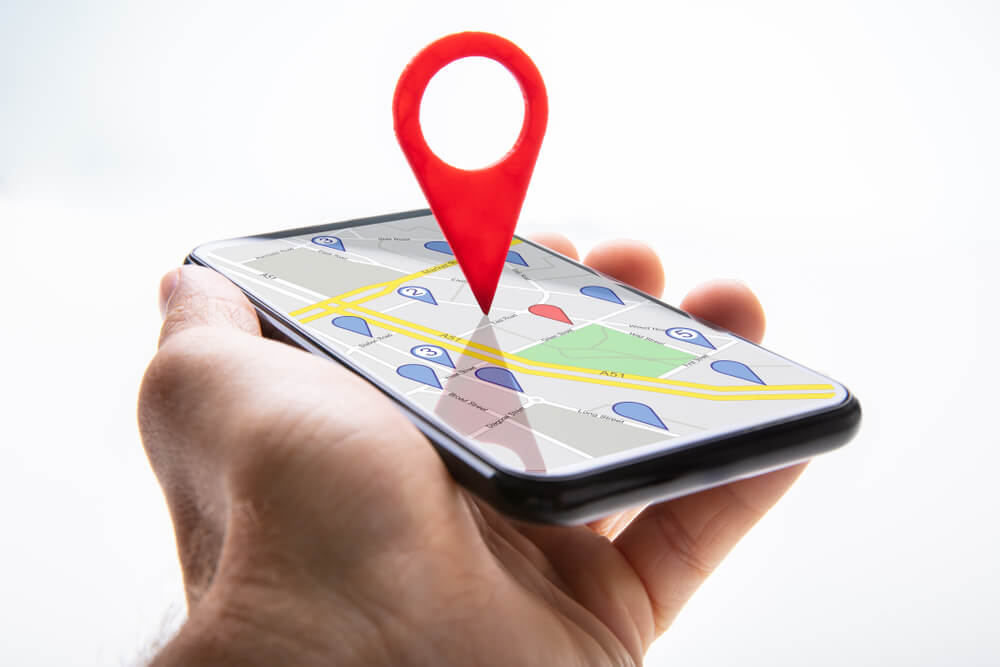 Close up of a Persons Hand Holding Cellphone With Red Map Pin Pointer Against White Background